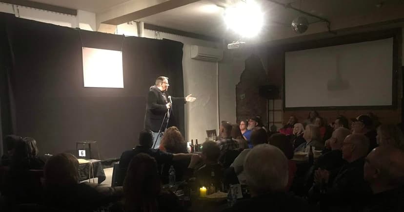 Eric Thompson commands the stage with his signature charm, captivating an intimate audience in this cozy comedy club setting where every seat in the house gets the full Thompson experience.