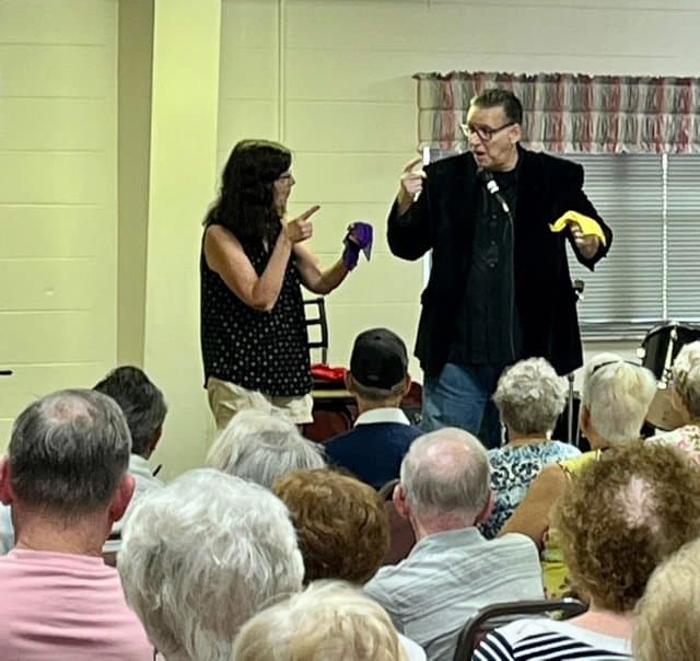 Eric Thompson captivates a packed audience as he performs his signature blend of comedy and magic, with an enthusiastic volunteer joining him on stage for what's sure to be a memorable trick.