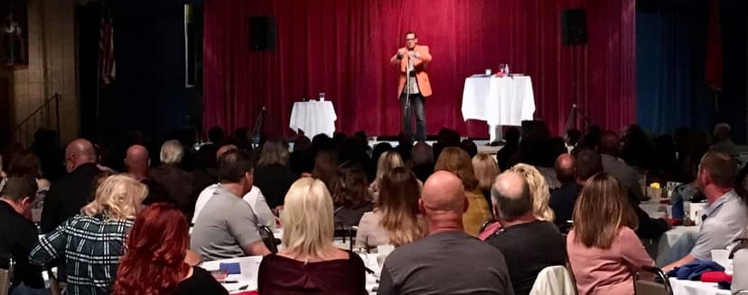 Eric Thompson commands the stage at a packed dinner theater event, delivering his signature blend of comedy and magic to an engaged audience enjoying their evening out.