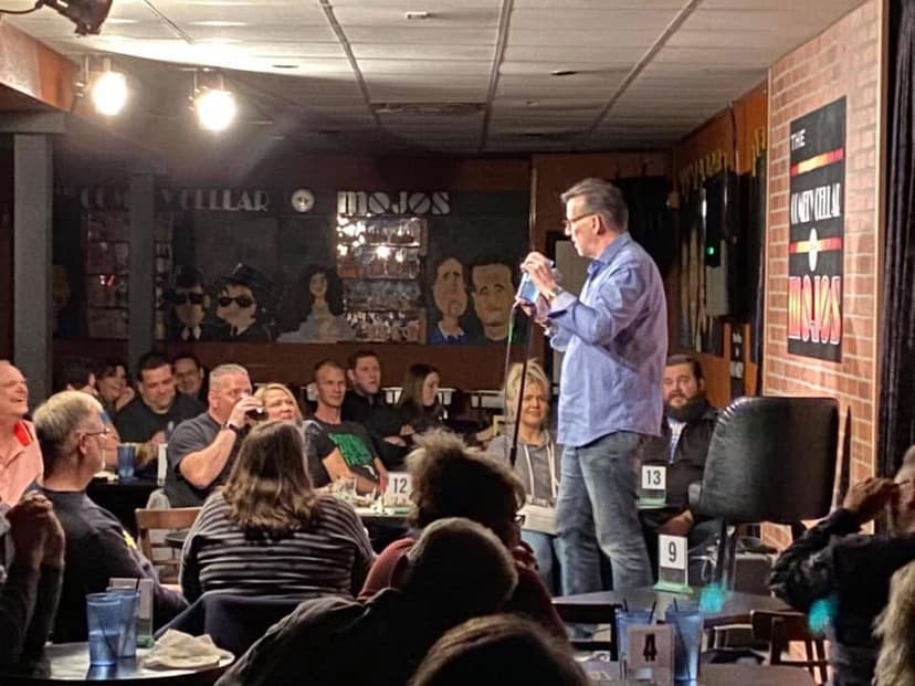 Eric Thompson commands the room at what appears to be a lively restaurant or comedy club event, microphone in hand as he engages with his seated audience. The intimate venue buzzing with laughter creates the perfect atmosphere for Eric's signature blend of comedy and magic.