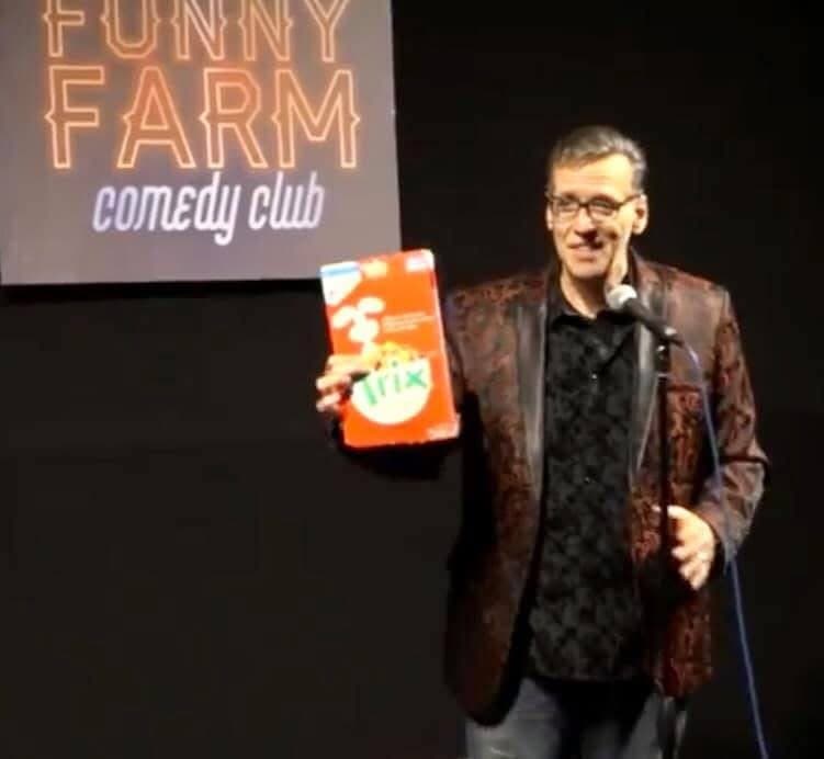 Eric Thompson takes the stage at Funny Farm Comedy Club, holding up what appears to be a colorful prop as part of his signature blend of comedy and magic that keeps audiences laughing.