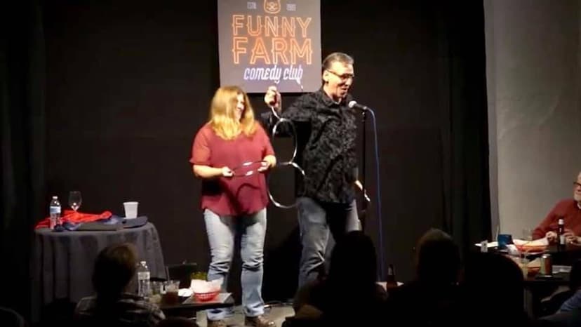 Eric Thompson brings a volunteer on stage for what looks like an interactive comedy bit at the Funny Farm Comedy Club, with the audience eagerly watching the fun unfold.