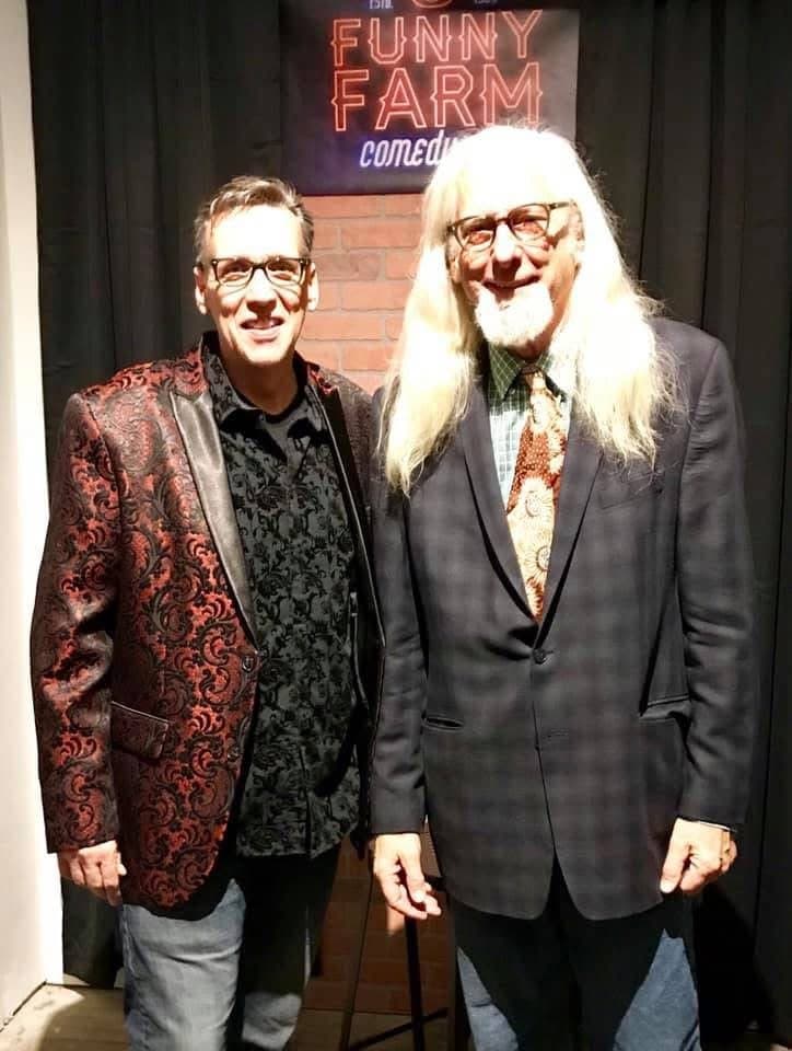 Eric Thompson poses with a fellow entertainer at the iconic Funny Farm comedy club, both sporting their signature stylish looks after what was likely a memorable night of laughs.