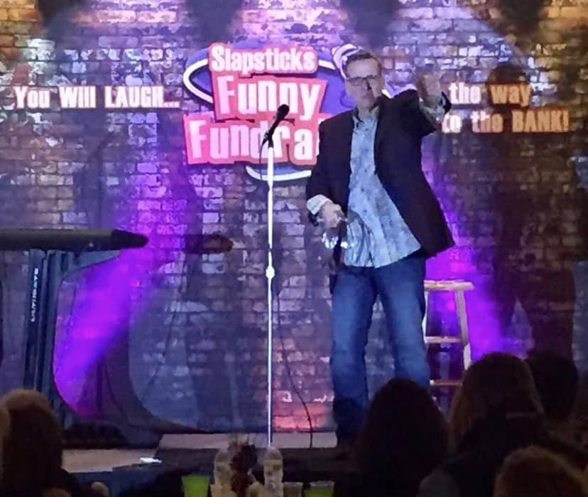 Eric Thompson brings down the house at Slapstick's Funny Fundra, delivering his signature blend of comedy and charm to a delighted audience in this intimate brick-walled venue.