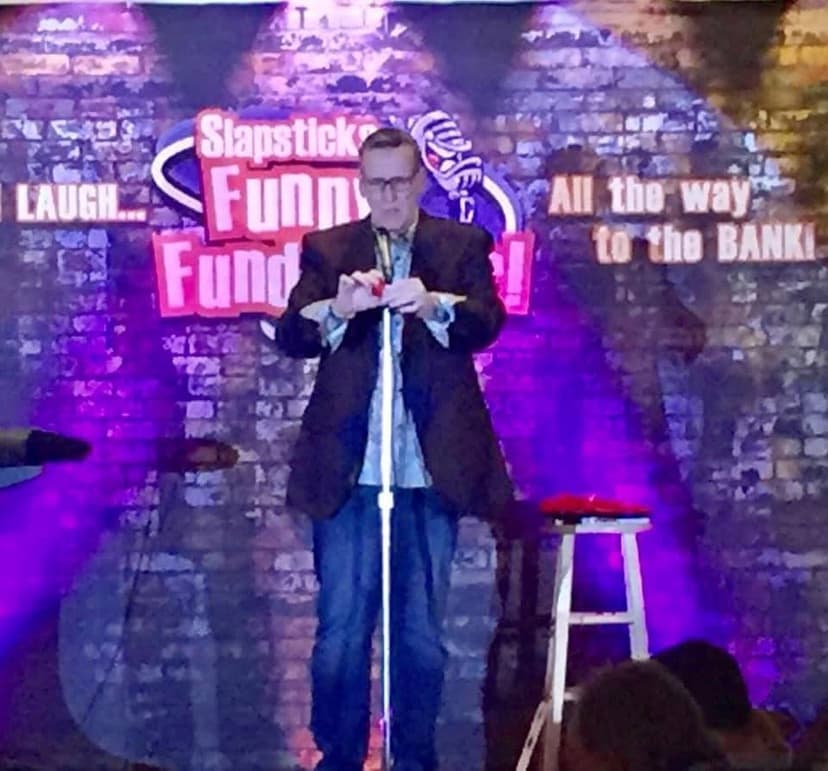 Eric Thompson takes the stage at a vibrant comedy club, commanding the microphone with his signature blend of humor and showmanship against the iconic brick wall backdrop.
