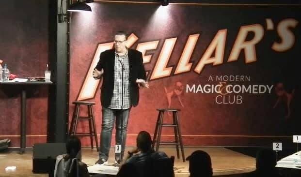 Eric Thompson takes the stage at what appears to be Hellar's Modern Magic Comedy Club, delivering his signature blend of comedy and magic to an intimate audience.