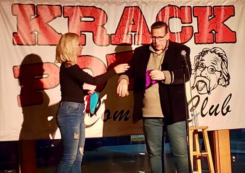 Eric Thompson charms the audience at a comedy club performance, sharing a lighthearted moment with a fan on stage while the crowd enjoys the interactive show.