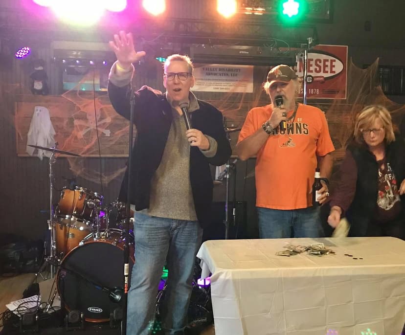 Eric Thompson commands the stage with characteristic enthusiasm, waving to the crowd while sharing the spotlight with fellow performers at what appears to be a lively fundraiser or community event.