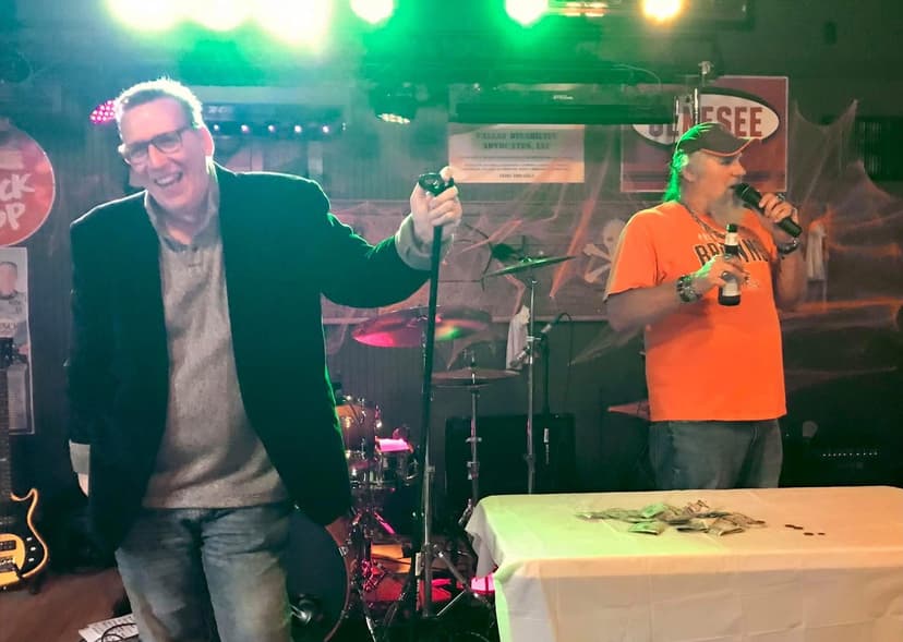 Eric Thompson shares the stage with a fellow performer at what appears to be a lively club venue, both entertainers clearly enjoying the moment as they work the crowd together.