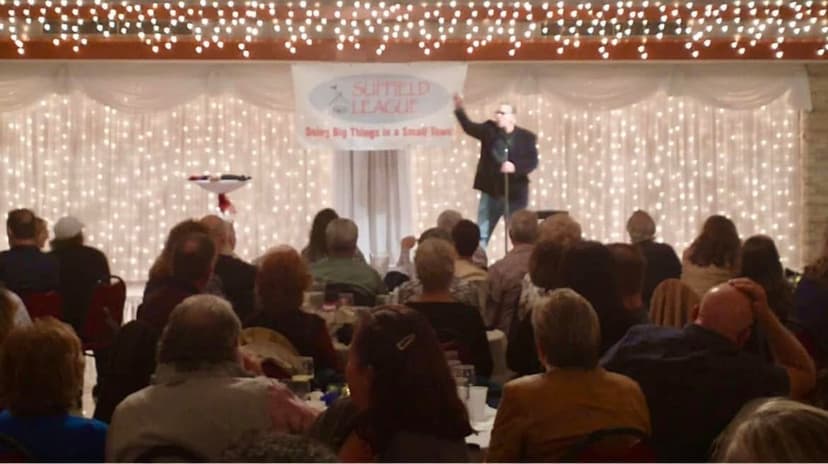 Eric Thompson commands the stage at a festive banquet hall event, entertaining a packed audience under twinkling string lights that create the perfect atmosphere for an evening of laughter and magic.