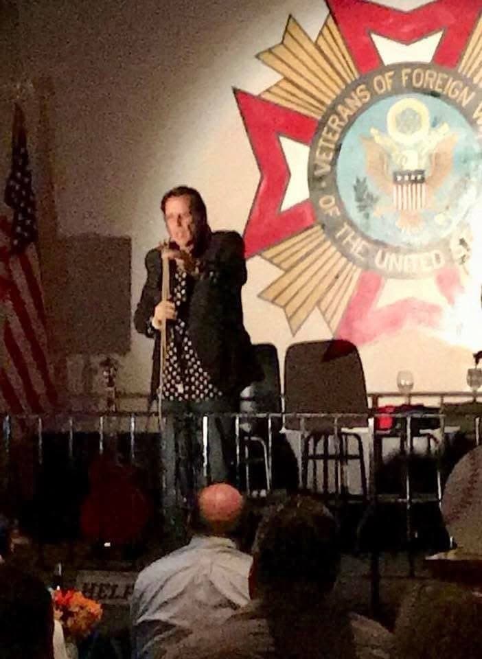 Eric Thompson commands the stage at what appears to be a Veterans of Foreign Wars event, bringing his signature blend of comedy and magic to honor our nation's heroes.