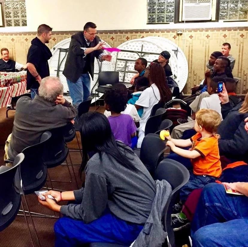 Eric Thompson captivates a diverse audience gathered in what appears to be a church or community center, with his signature white backdrop setup drawing everyone's attention during this intimate performance.