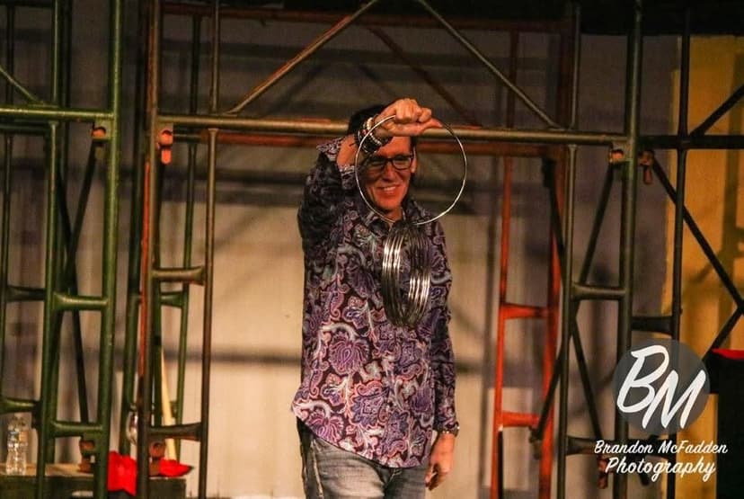 Eric Thompson demonstrates his magical prowess with metal linking rings, showcasing the classic illusion that has captivated audiences for generations. The seasoned performer works his magic against an industrial backdrop, proving that entertainment can transform any space into a theater of wonder.