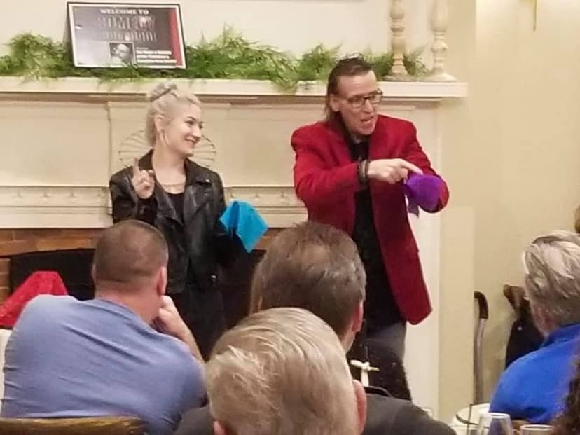 Eric Thompson delights an intimate audience with his signature blend of comedy and magic, while a young assistant shares in the laughter during what appears to be a cozy venue performance.