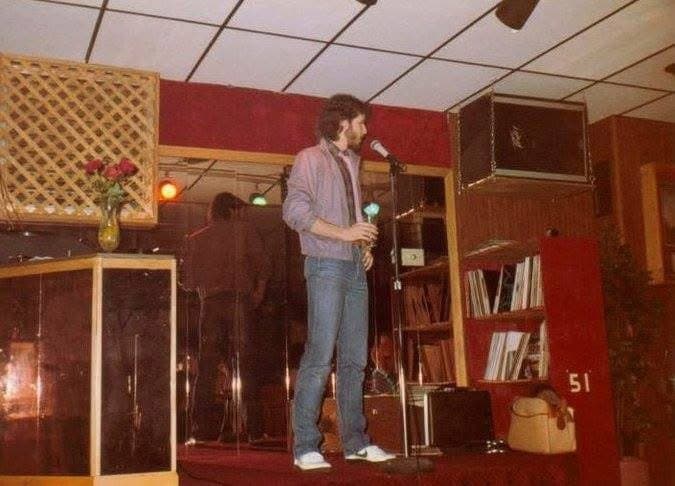Eric Thompson takes the stage at what appears to be an intimate comedy club venue, microphone in hand and ready to deliver his signature blend of humor and entertainment to the audience.