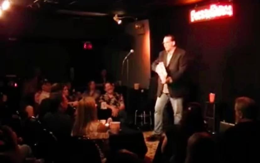 Eric Thompson commands the stage at an intimate comedy club, working his magic on a captivated audience in the dimly lit venue.