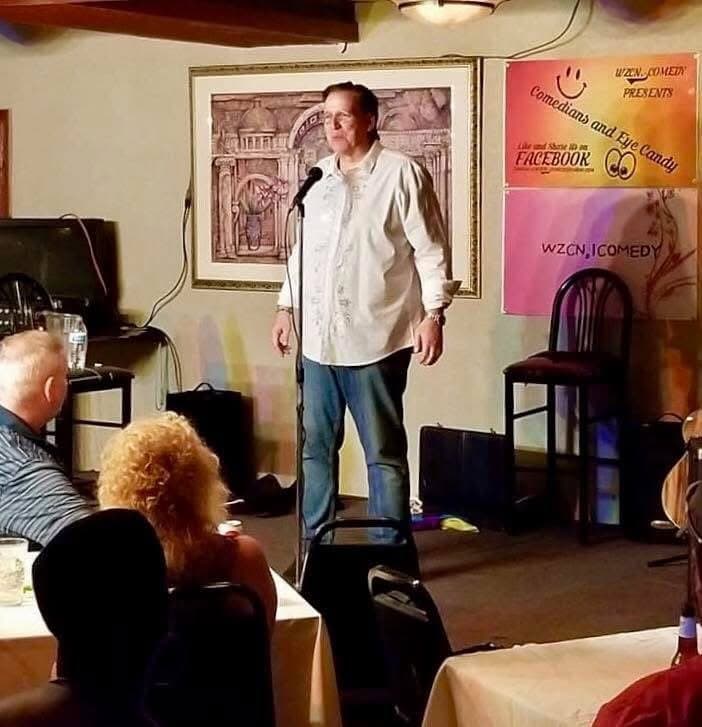 Eric Thompson commands the stage at an intimate comedy venue, delivering his signature blend of humor to an appreciative audience in what appears to be a cozy restaurant or comedy club setting.