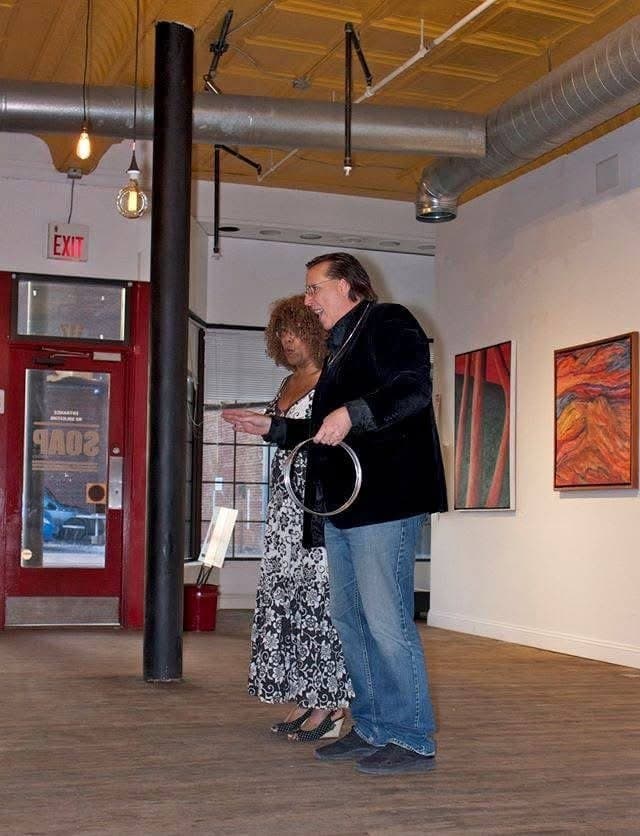 Eric Thompson shares an intimate moment with an audience member at what appears to be an art gallery or cultural venue, creating the kind of personal connection that makes his performances so memorable.