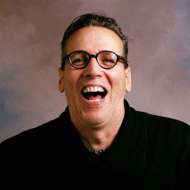 Eric Thompson flashes his signature infectious smile and hearty laugh during what appears to be a professional photo session, showcasing the warm, approachable personality that has made him a favorite entertainer for decades.