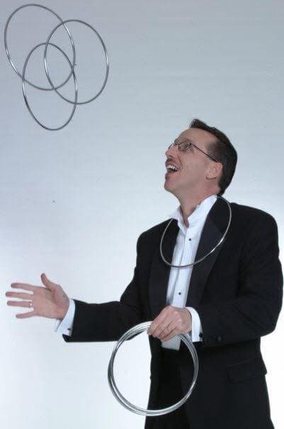 Eric Thompson showcases his juggling prowess with metal rings, flashing his signature smile as he demonstrates the precision and showmanship that has made him a sought-after entertainer for decades.